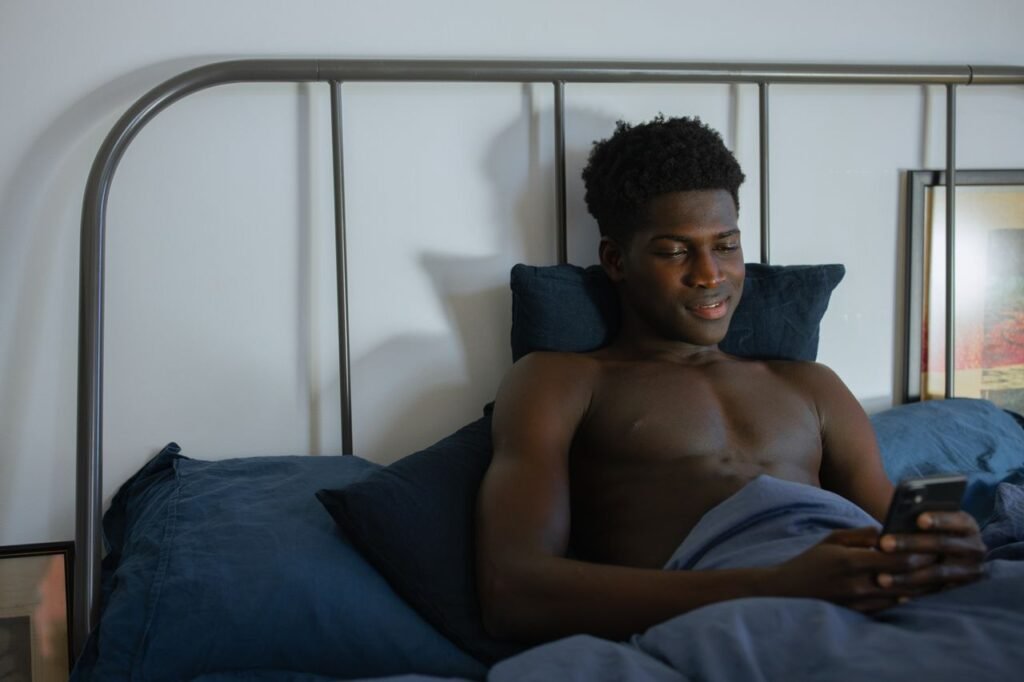 Young adult man relaxing in bed using his smartphone, enjoying a peaceful evening at home.